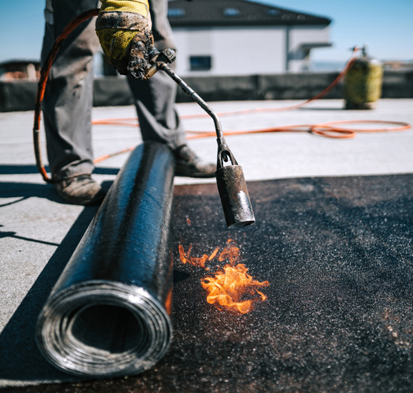 Professional workers insulating rooftop with bitumen membrane.